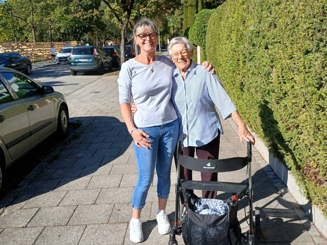 Betreuerin von Curatum Familia begleitet eine Seniorin mit Rollator bei einem Spaziergang durch die Nachbarschaft